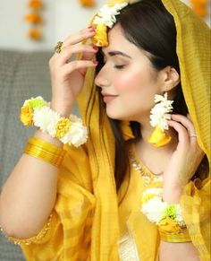 a woman with flowers in her hair wearing a yellow sari and holding two bracelets