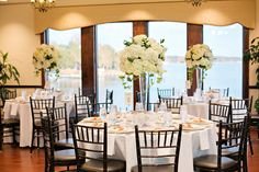 the tables are set with white flowers and place settings for an elegant wedding reception in front of a large window