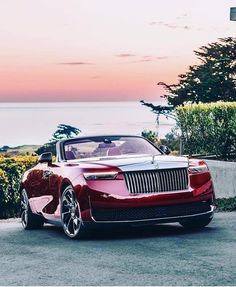 a red convertible car parked in front of a house near the ocean at sunset or dawn