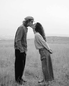 black and white photograph of two people kissing each other in an open field with mountains in the background