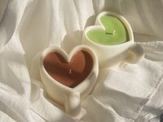 two heart shaped candles sitting next to each other on a white cloth covered bed sheet