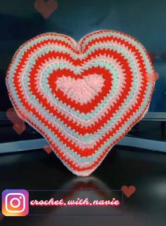 a crocheted heart sitting on top of a tv screen with hearts in the background