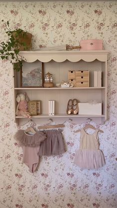 two baby clothes are hanging on the wall next to a shelf with books and toys