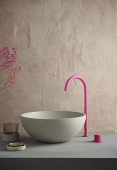 a white bowl sitting on top of a counter next to a pink vase with flowers