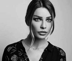 a black and white photo of a woman with long hair wearing a floral shirt looking at the camera