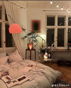 an unmade bed with white sheets and pillows in front of two windows, surrounded by plants