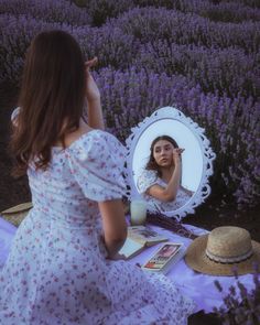 a woman is looking at her reflection in the mirror while sitting on a lavender field