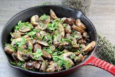 a pan filled with mushrooms and parsley on top of a wooden table next to a red spatula