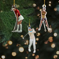 three ornaments hanging from a christmas tree in the shape of women playing golf, one holding a club