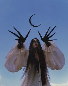 a woman with long hair and two hands on her head, standing in front of the moon