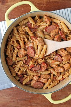 a pot filled with pasta and sausage on top of a wooden table