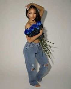 a woman with flowers in her hands posing for the camera while wearing ripped jeans and heels