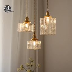 three lights hanging from a ceiling with flowers in the foreground and curtains behind them