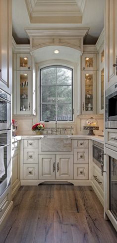 a kitchen with white cabinets and wood flooring next to an oven, sink, microwave and window