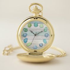 a gold pocket watch with blue and green numbers on the face sits on a white surface