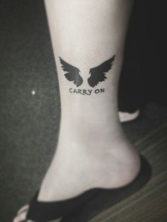 a person with a tattoo on their foot that says carry on and two black wings