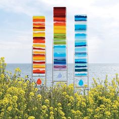 three tall metal sculptures with different colors on them in front of flowers and the ocean