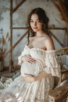 a pregnant woman sitting on a chair with her arms wrapped around her belly and wearing a white dress