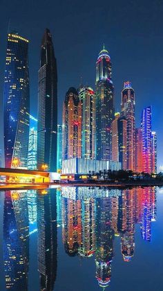 the city is lit up at night and reflecting in the water