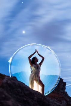 a woman standing on top of a rocky hill under a blue sky and moon filled sky