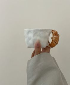 a hand holding a small white cup with a knot in it's middle, on a plain background