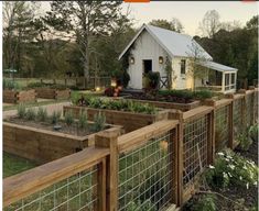 a small white house surrounded by lots of plants and flowers in a garden with wooden fences