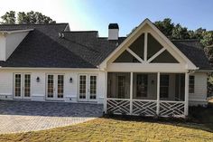 a white house with black shingles and windows on the front porch is surrounded by green grass