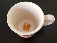 a small brown dog sitting inside of a white cup on top of a black table