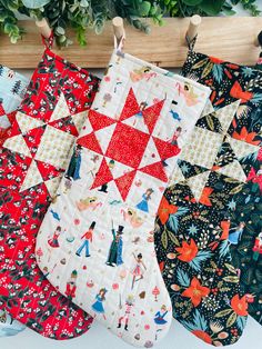 four quilted christmas stockings hanging on a wooden rack with greenery in the background