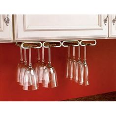 four wine glasses hanging from the wall in a kitchen with red walls and white cabinets