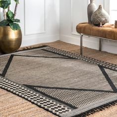 an area rug with black and white designs on it in front of a bench, potted plant and window