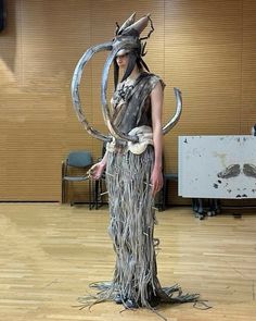 a woman in an elaborate costume standing on a hard wood floor with a large metal object around her neck