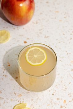 an apple sits next to a glass of lemonade and some sliced up lemons