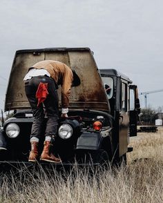 a man standing on the hood of an old pickup truck in a field with tall grass