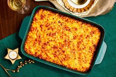 a green casserole dish with cheese on it next to some wine glasses and utensils