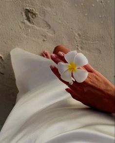 a woman's hand holding a flower on top of a white sheet