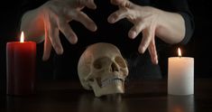 a human skull sitting on a table next to two burning candles and a candle holder