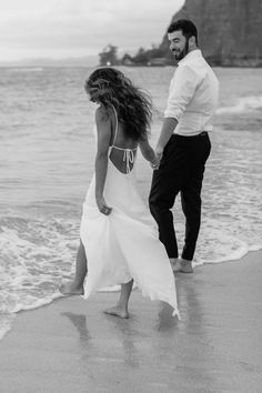 a man and woman walking on the beach holding hands