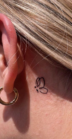 a close up of a person with a small tattoo on their behind the left ear