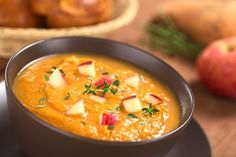 a bowl of soup on a plate next to some apples and other food in the background