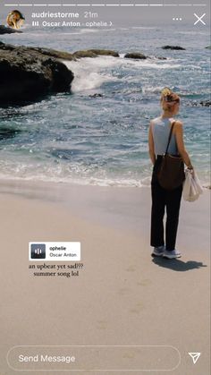 a woman standing on top of a sandy beach next to the ocean in front of rocks