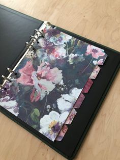 a black binder with flowers on it sitting on a wooden table next to a pen