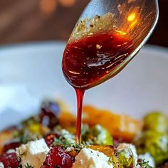 a spoon drizzling ketchup over a bowl of vegetables and cheese