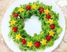 a white plate topped with a green wreath covered in lettuce and stars next to tomatoes