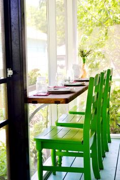 the green chairs are sitting on the porch by the table with plates and utensils