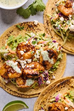 three tacos with shrimp, lettuce and cole slaw on them next to a bowl of salsa