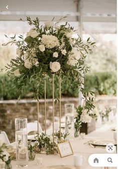 the centerpieces on this table are all white flowers and greenery in gold vases