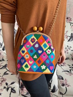 a woman is holding a colorful purse in her hands and wearing brown sweater with flowers on it