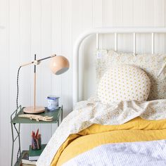 a bed with yellow and white sheets on it, next to a small table with pencils