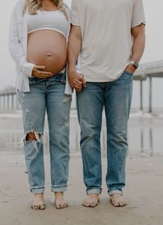 a pregnant man and woman standing next to each other on the beach with their belly exposed